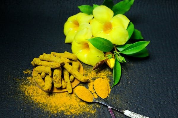 Pó de cúrcuma amarelo-alaranjado trás contrate com fundo cinza escuro do prato e para compor o retrato foi adicionado um linda flor amarelo com caule verde.